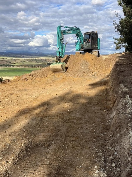 An excavator shaping earth on a rural block