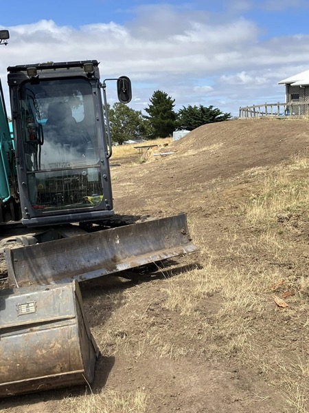 An excavator cutting into a bank beside a building
