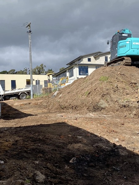 An excavator on a large dirt mound with a home behind