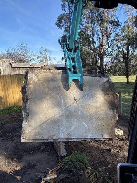 An excavator lifting a broken concrete slab during demolition