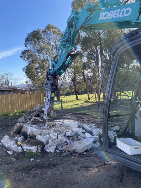 An excavator with a hydraulic breaker splitting rock