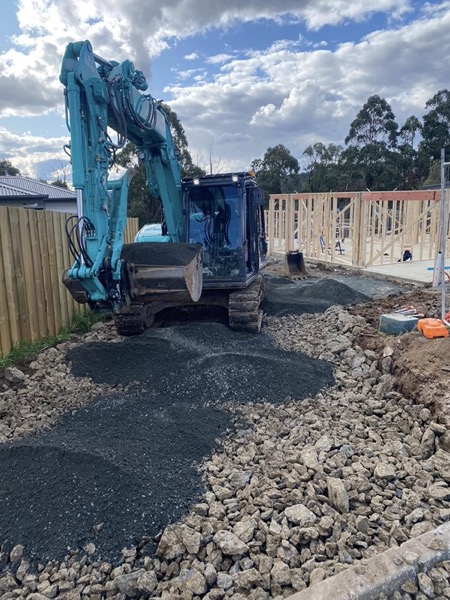 A Tolman Services excavator on rocky ground beside framing
