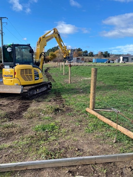 An excavator working on a green rural block with fence posts